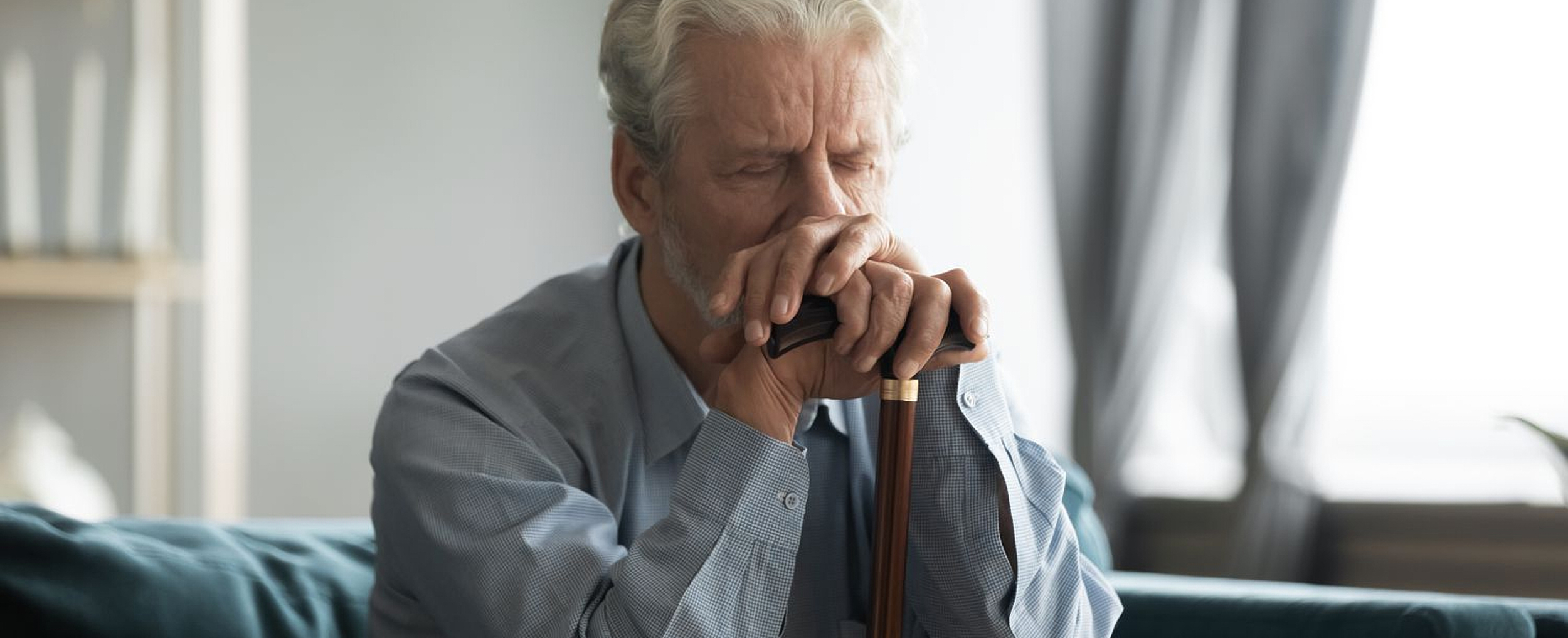 An elderly man with his brow furrowed in pain, holding a cane for support.
