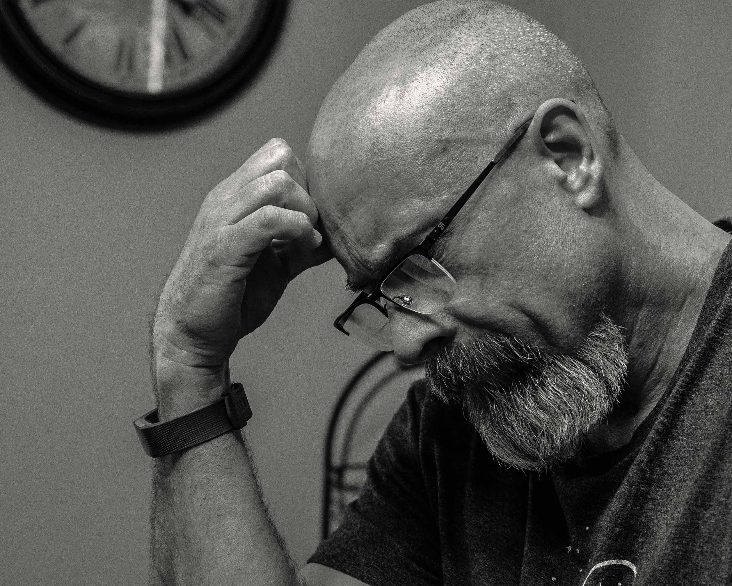 A close-up image of a black-and-white image of a man looking down with his closed hand on his forehead.