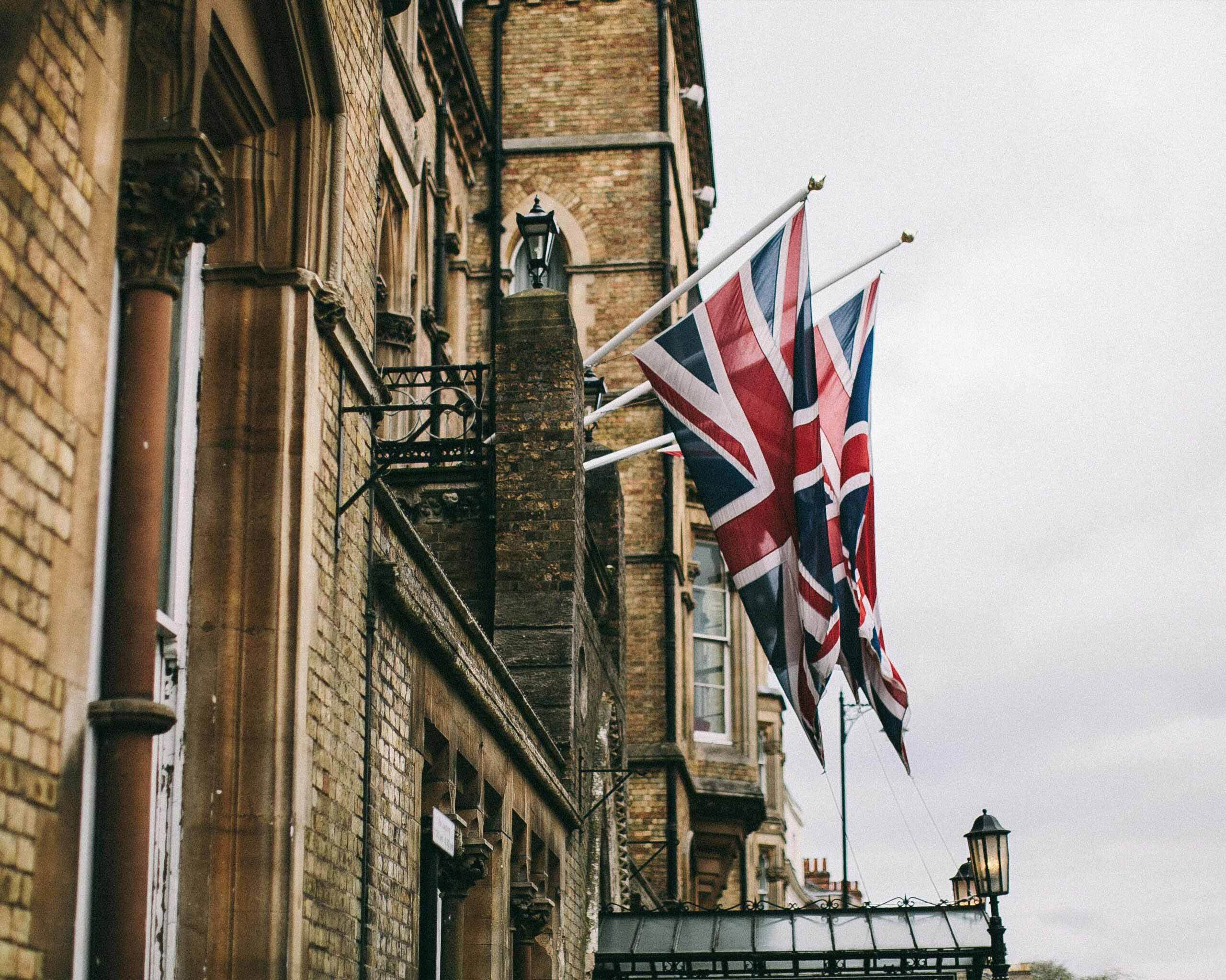 Two union jack flags hang from the side of an old brick building.